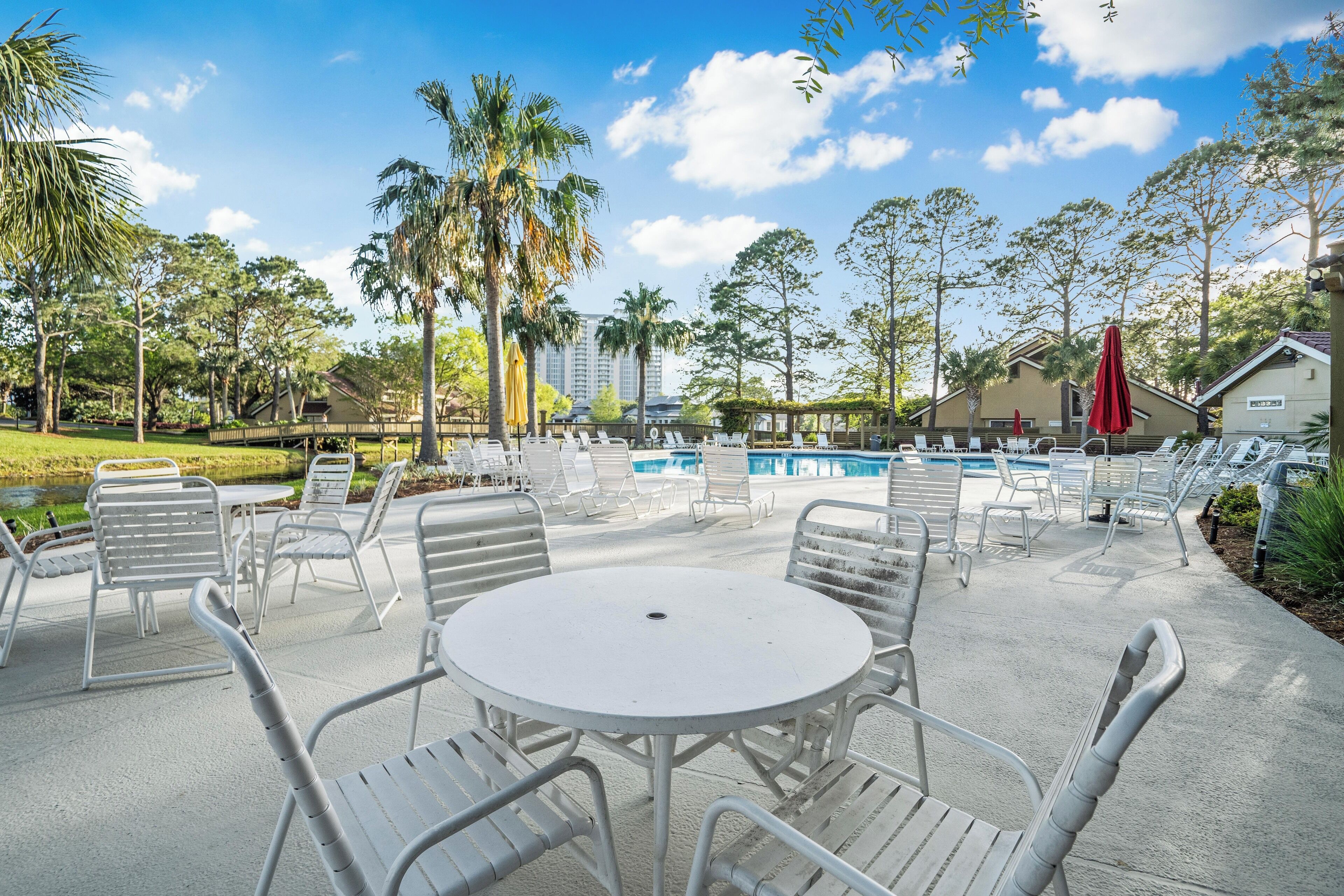 A poolside area with lounge chairs, a table, and a view of a building in the background.