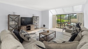A living room with a sofa, coffee table, TV, and bookshelf. - 3 Pools - PET FRIENDLY - Gulfside of Sandestin Resort (Miramar Beach)