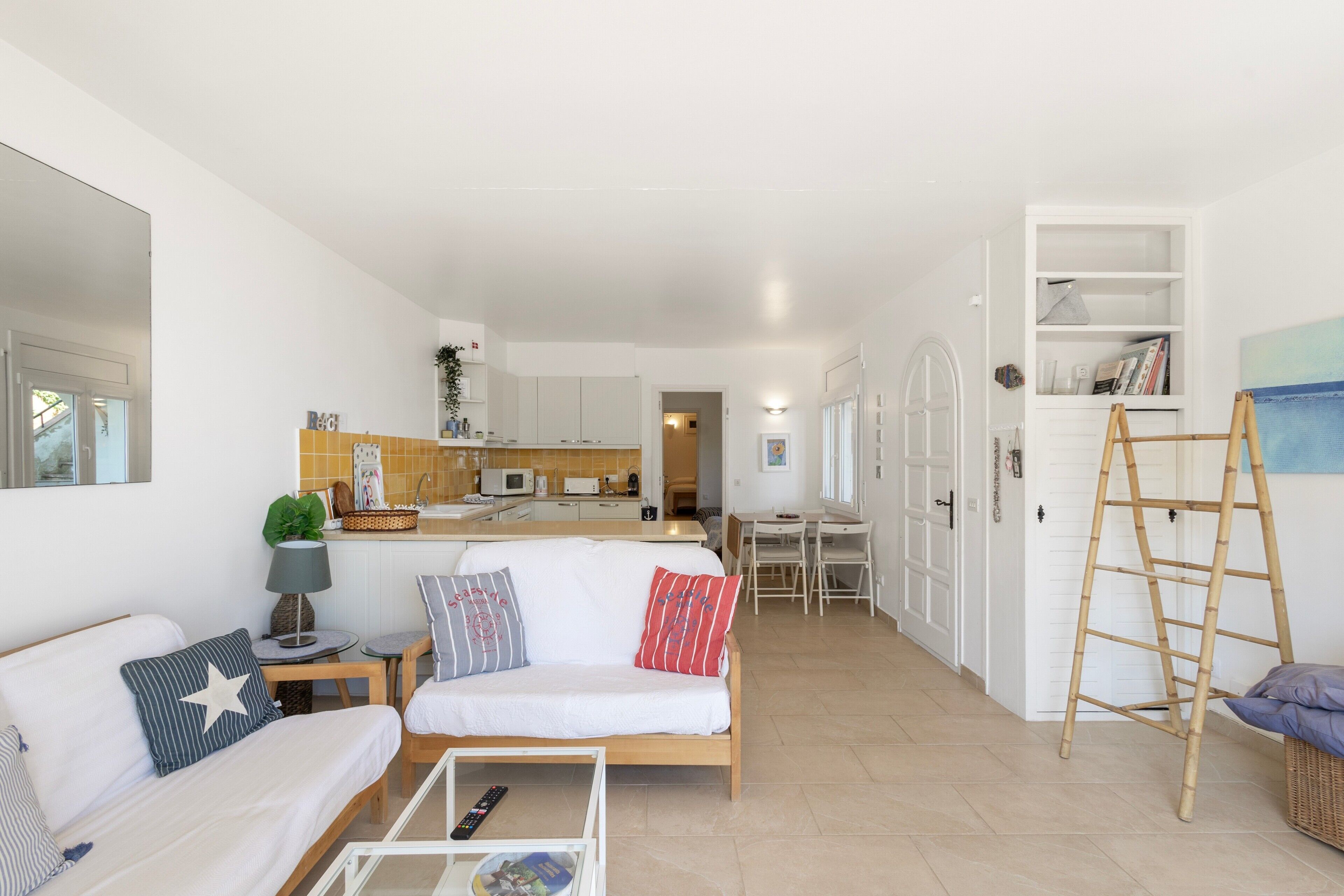 A compact living space with a sofa, a small table, a ladder, and a kitchenette in the background.