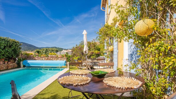 Zona junto a la piscina con mesa lista para comer, un banco azul y vista al estanque.
