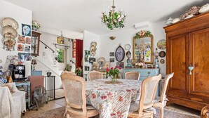 Un comedor con una mesa dispuesta para cuatro personas, rodeada de sillas de mimbre, una araña y un aparador de madera.