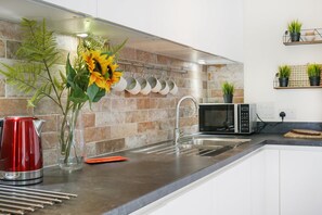 A modern kitchen with a stainless steel sink, a microwave, and a vase with sunflowers. - Stylish 2-Bed Flat Near Central London (London)