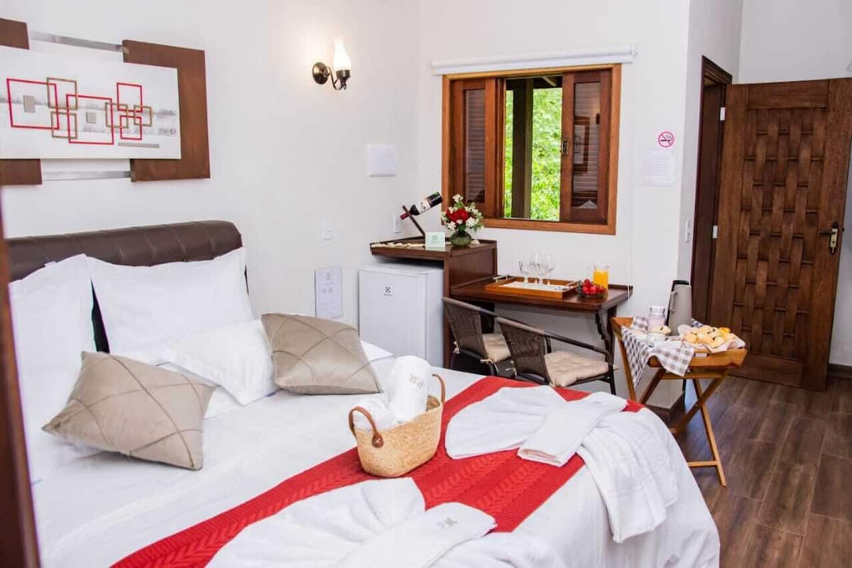 A hotel room with a bed, a desk, a window, and a door.