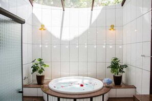 Um banheiro com banheira, duas luminárias na parede e plantas em vasos.