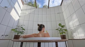 A person in a bathtub with tiled walls and potted plants. - Pousada Medeiros  (Monte Verde)