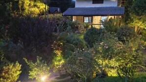 A two-story house with a tiled roof, surrounded by lush greenery and a garden. - Pousada Medeiros  (Monte Verde)