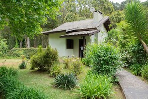 A small, single-story building with a tiled roof, surrounded by lush greenery and a pathway leading to the entrance. - Pousada Medeiros  (Monte Verde)