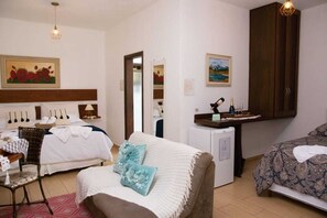 Quarto de hotel com cama, escrivaninha, cadeira, pequeno frigorífico e armário.