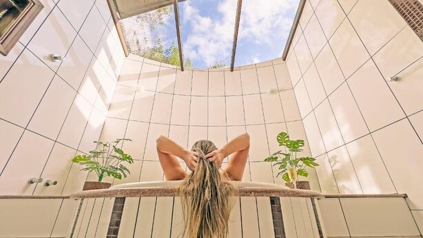 A person seated on a bench in a sunlit room with tiled walls and potted plants. - Pousada Medeiros  (Monte Verde)