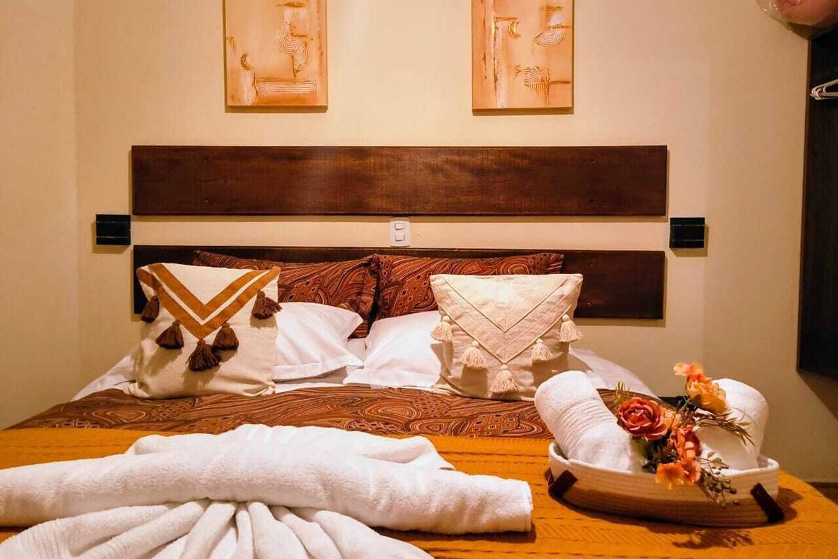 A neatly made bed with pillows, a blanket, and a floral arrangement on a wooden bed frame.