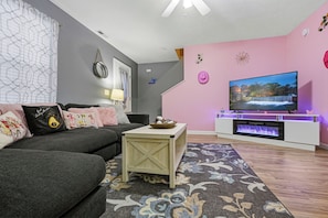 A modern living room with a grey sofa, a wooden coffee table, a flat-screen TV, and a fireplace. - Sevierville | Dolly Themed | Close to Dollywood (Sevierville)