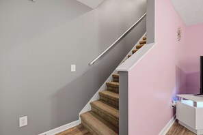 En trappa med ett träräcke, en vit vägg och en rosa vägg med en dekorativ detalj.