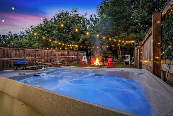 A hot tub with a fire feature, surrounded by a wooden fence and string lights. - Sevierville | Dolly Themed | Close to Dollywood (Sevierville)