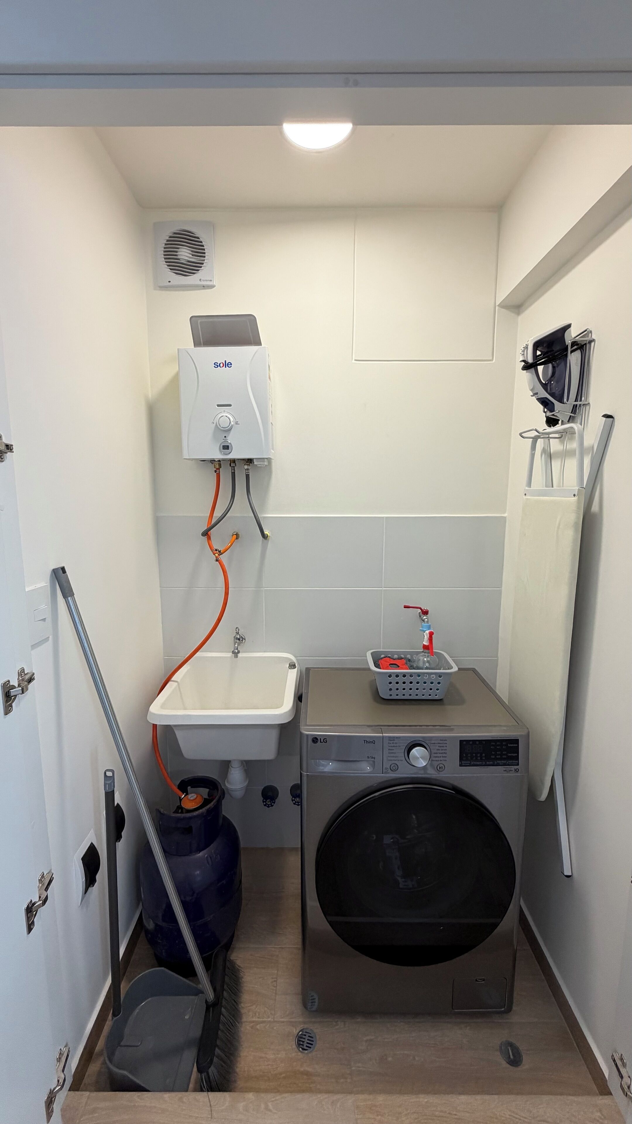 A compact laundry room with a washing machine, a sink, and a heater.
