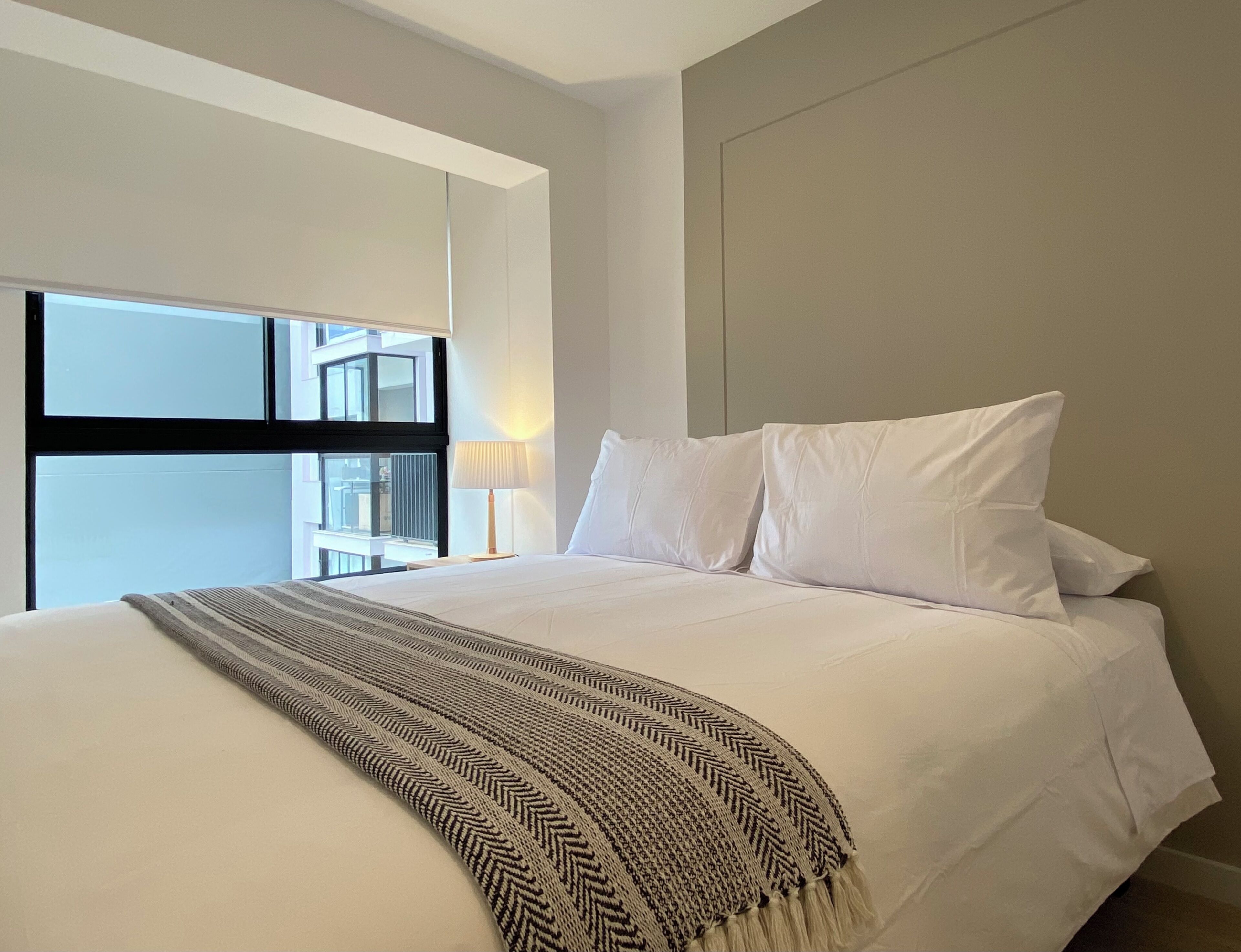 A modern hotel room with a large bed, a view of the city, and a window with blinds.