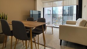 A modern living room with a wooden dining table, grey chairs, a beige sofa, and a large sliding glass door leading to a balcony. - Amme by Wynwood House (Lima)