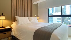 A hotel room with a bed, bedside lamps, a nightstand, a window with a city view, and a wooden panel wall. - Amme by Wynwood House (Lima)