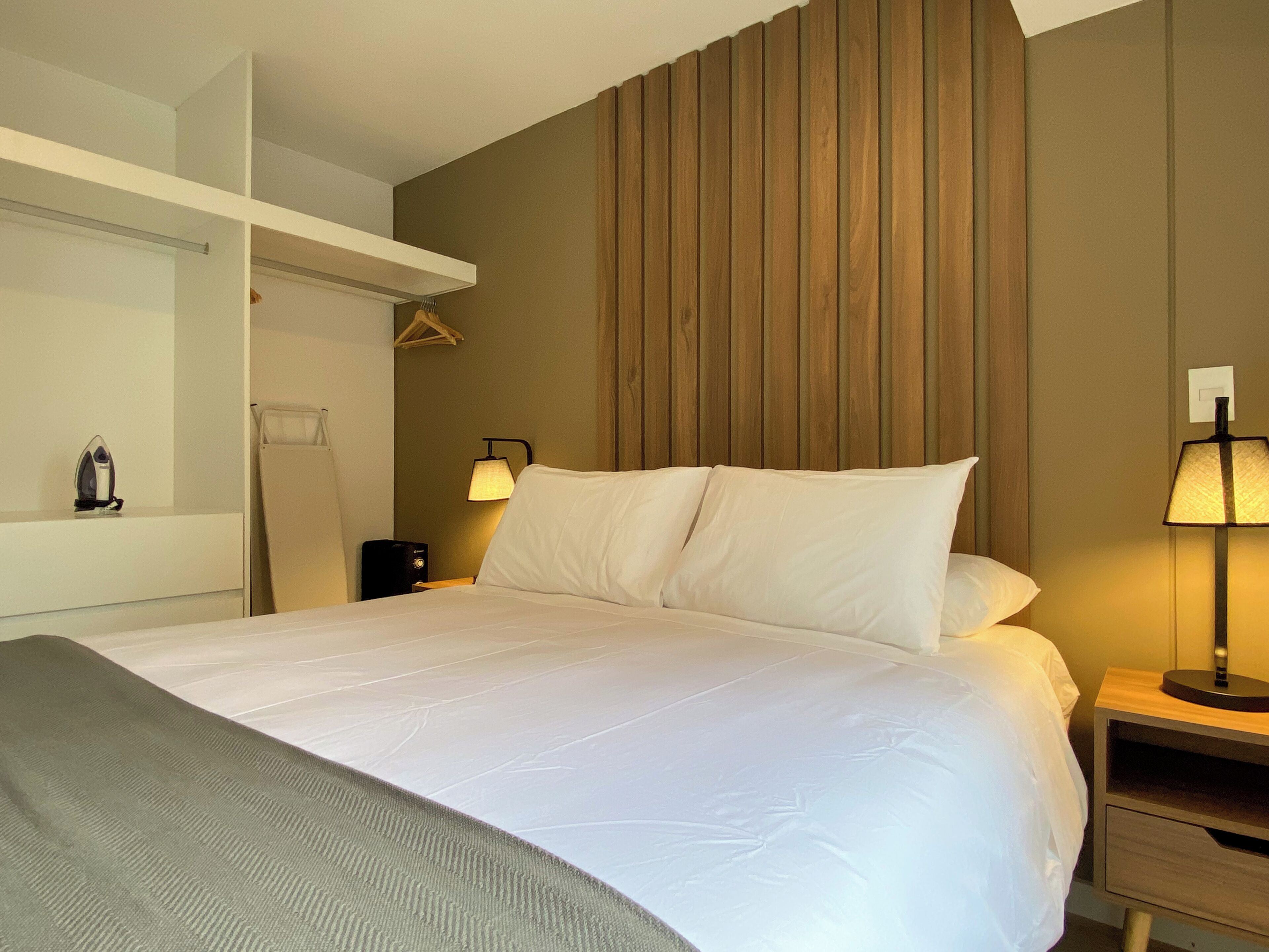 A neatly made bed with white linens, a bedside table with a lamp, and a wooden panel wall.