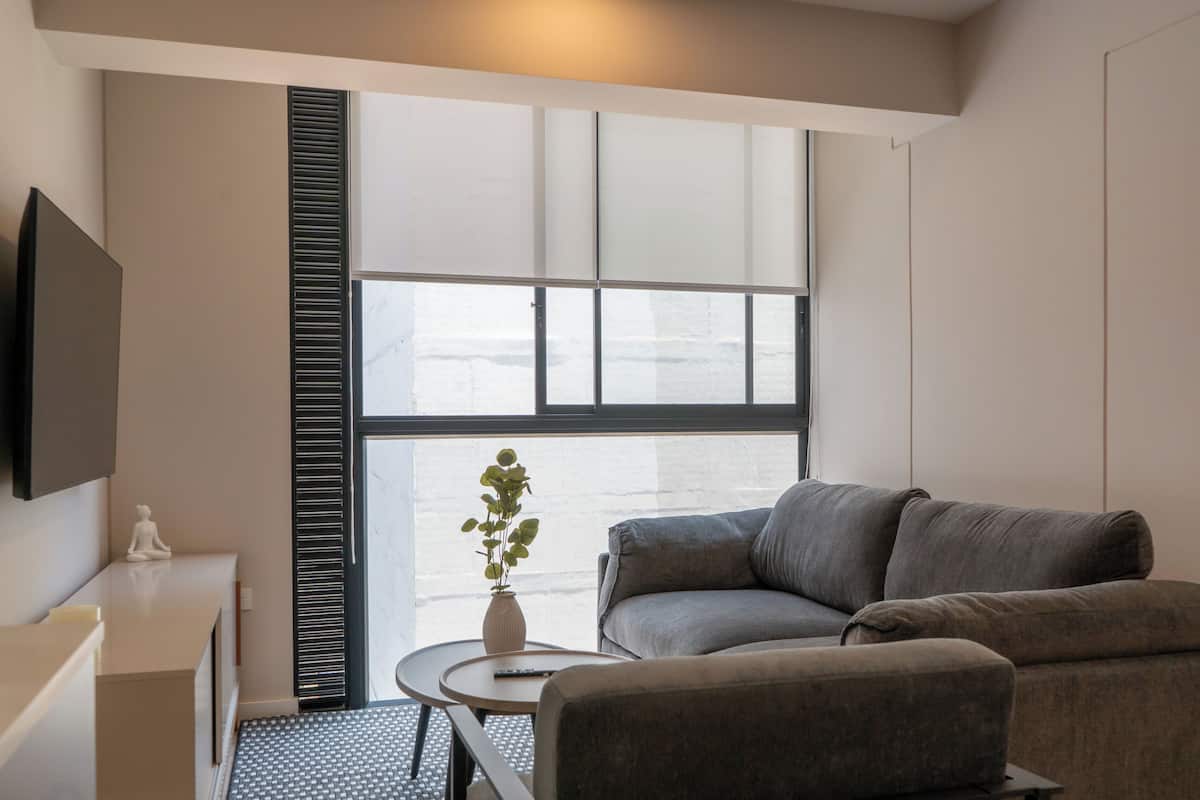 Une pièce moderne avec un canapé, une petite table sur laquelle est posé un vase, et un téléviseur fixé au mur.