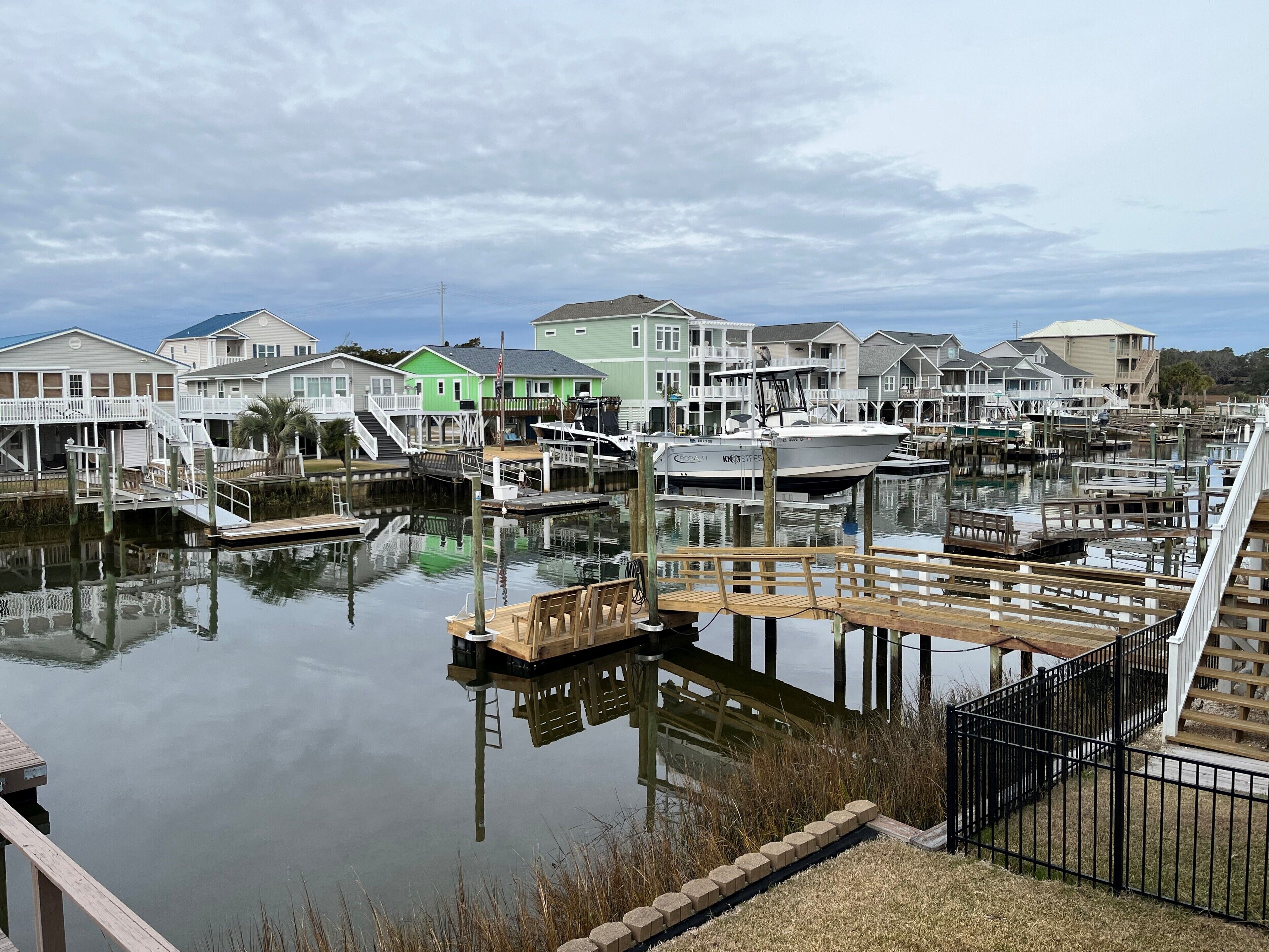 A marina with docked boats, a wooden pier, and houses with balconies.