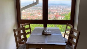 Un comedor con una mesa y sillas, un ventanal con vista a un paisaje urbano y techo de madera.