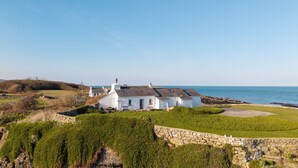 Ein Haus an der Küste mit einer Steinwand, einem Rasen und Blick auf das Meer.