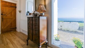 Eine Holztür, eine Kommode mit Schubladen, eine Lampe und Meerblick durch ein Fenster.