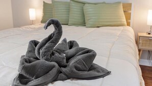 Una cama bien hecha con una toalla doblada en forma de cisne, una almohada verde y una lámpara de noche.