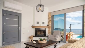 Uma sala de estar moderna com lareira, um sofá, uma mesa de centro e vista para o mar.
