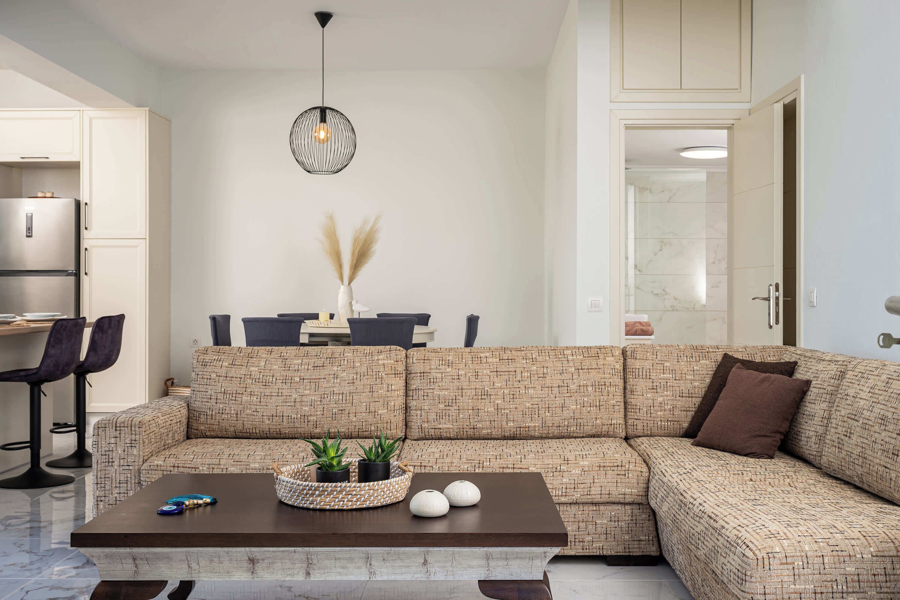 A modern living room with a sectional sofa, a coffee table, a dining area with chairs, and a kitchen area with a refrigerator.