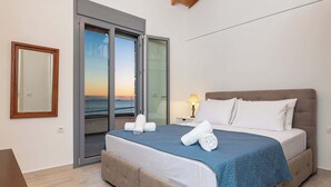Um quarto com uma cama, uma mesinha de cabeceira, uma luminária, uma porta de vidro deslizante e vista para o pôr do sol.