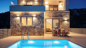 Um edifício moderno com fachada de pedra, piscina e área de estar ao ar livre.