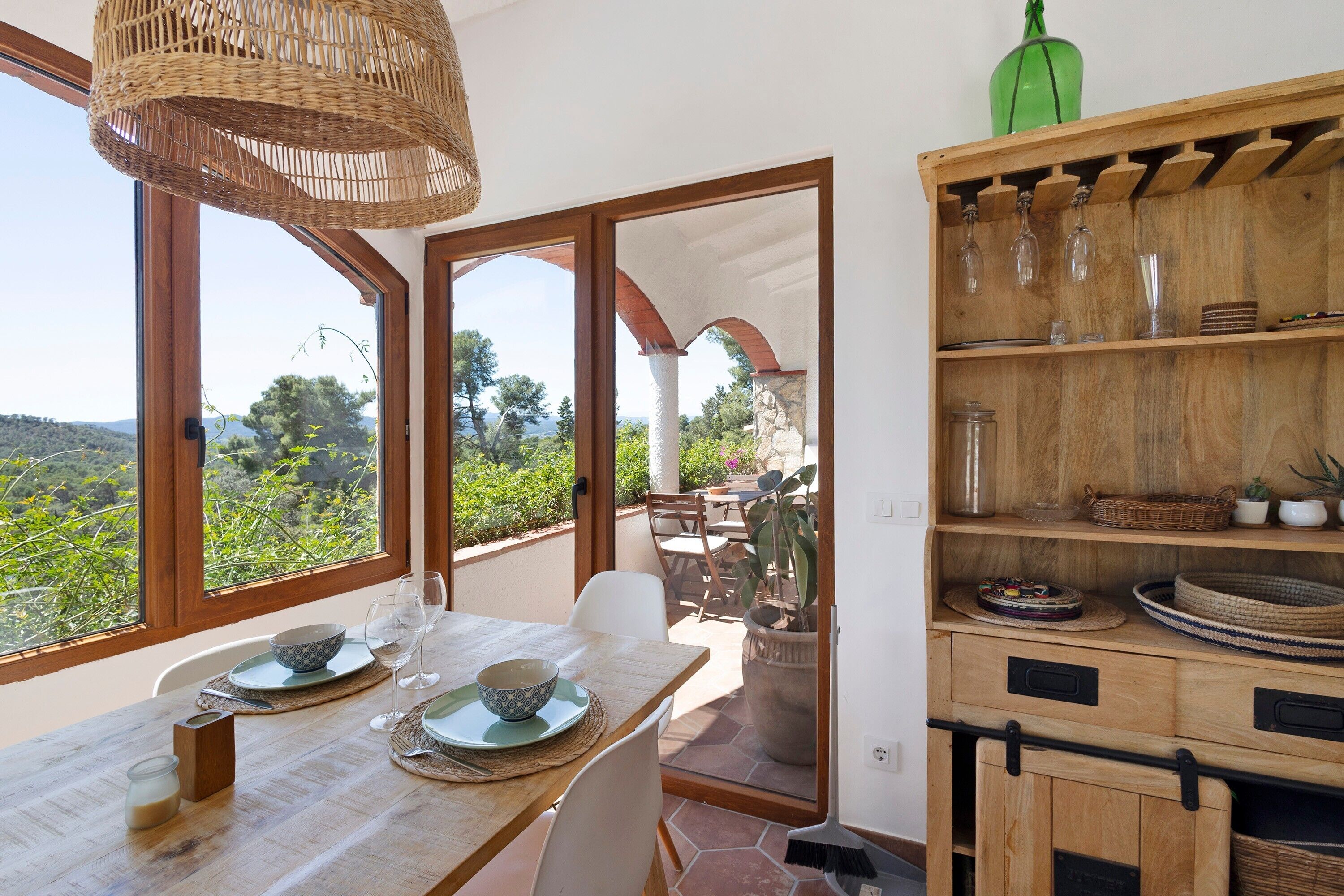 A dining area with a table set for two, a wicker chandelier, and a view of the outdoors.