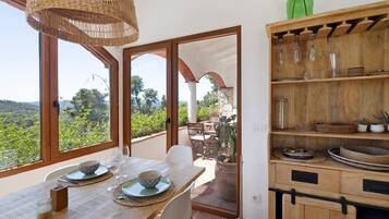 A dining area with a table set for two, a wicker chandelier, and a view of the outdoors.