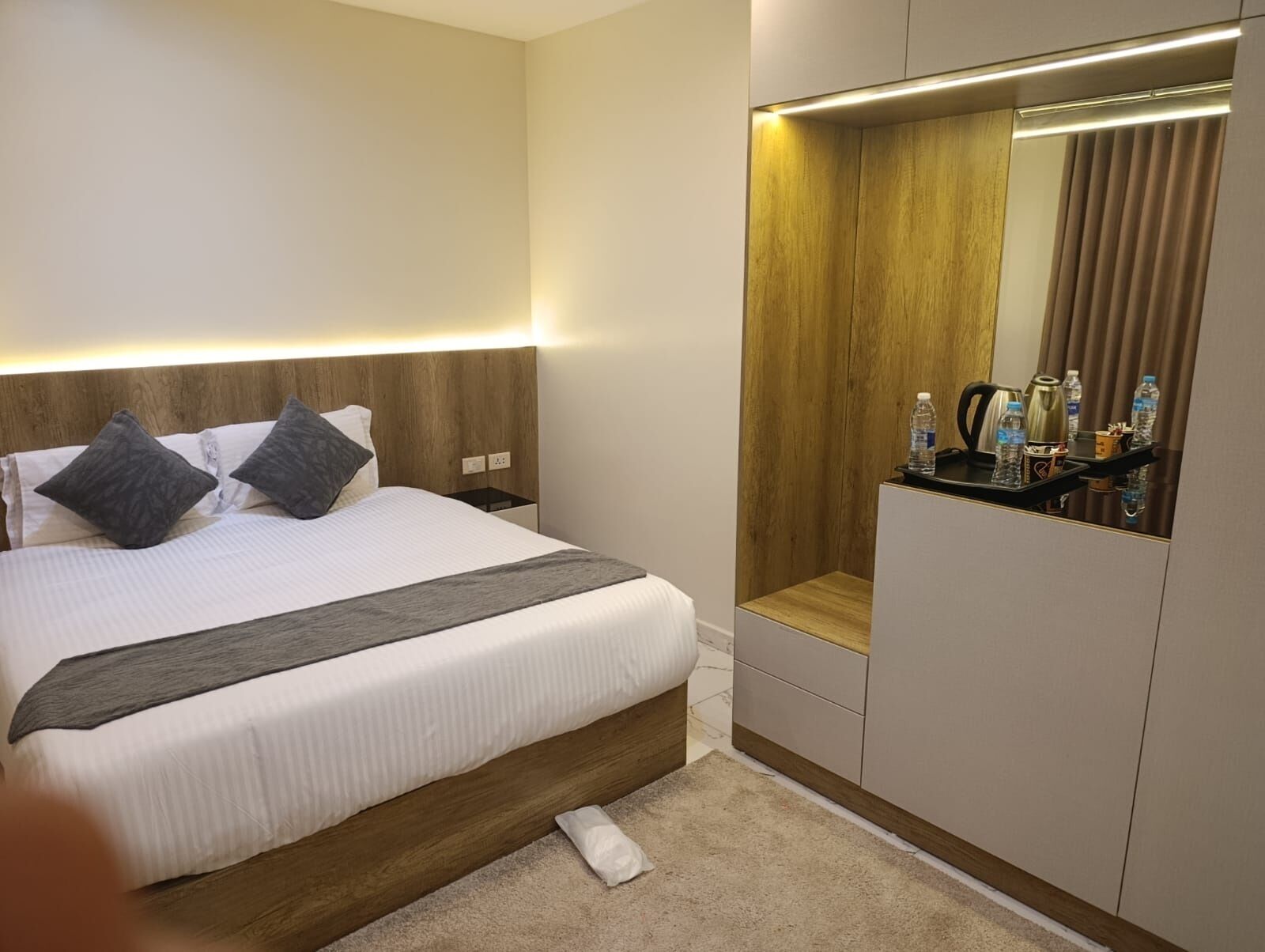 Habitación de hotel con cama, mesita de noche, espejo y un pequeño rincón de descanso.