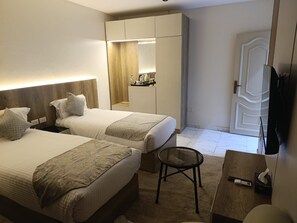 A hotel room with two beds, a small round table, a mirror, and a wardrobe. - Tamaya Hotel Fifth Settlement (Shurtah al-Dakhlah)