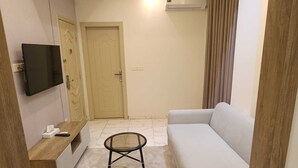 Una sala de estar con un sofá, un televisor montado en la pared, una puerta y un aire acondicionado.