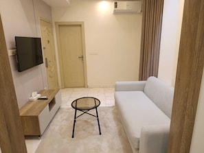 Una sala de estar con un sofá, un televisor montado en la pared, una puerta y un aire acondicionado.