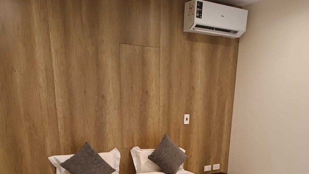 Un dormitorio con cabecera de madera, una cama con ropa blanca y dos almohadas, una mesita de noche y un equipo de aire acondicionado.