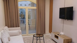 Una sala de estar moderna con un sofá, una mesita, un televisor montado en la pared y un ventanal corredero que da a un espacio exterior.