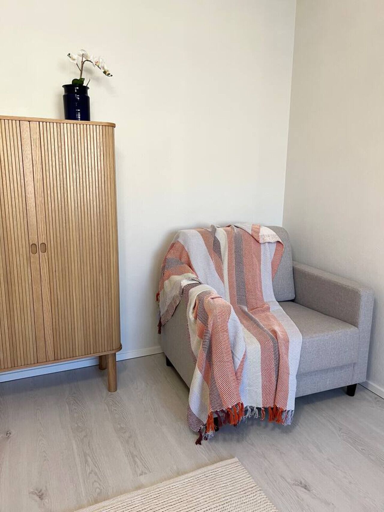 A room with a wooden wardrobe, a grey sofa, and a patterned throw blanket.