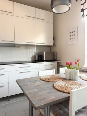 Una cocina moderna con armarios blancos, encimera negra y una mesa de comedor con individuales tejidos y tulipanes rosas.