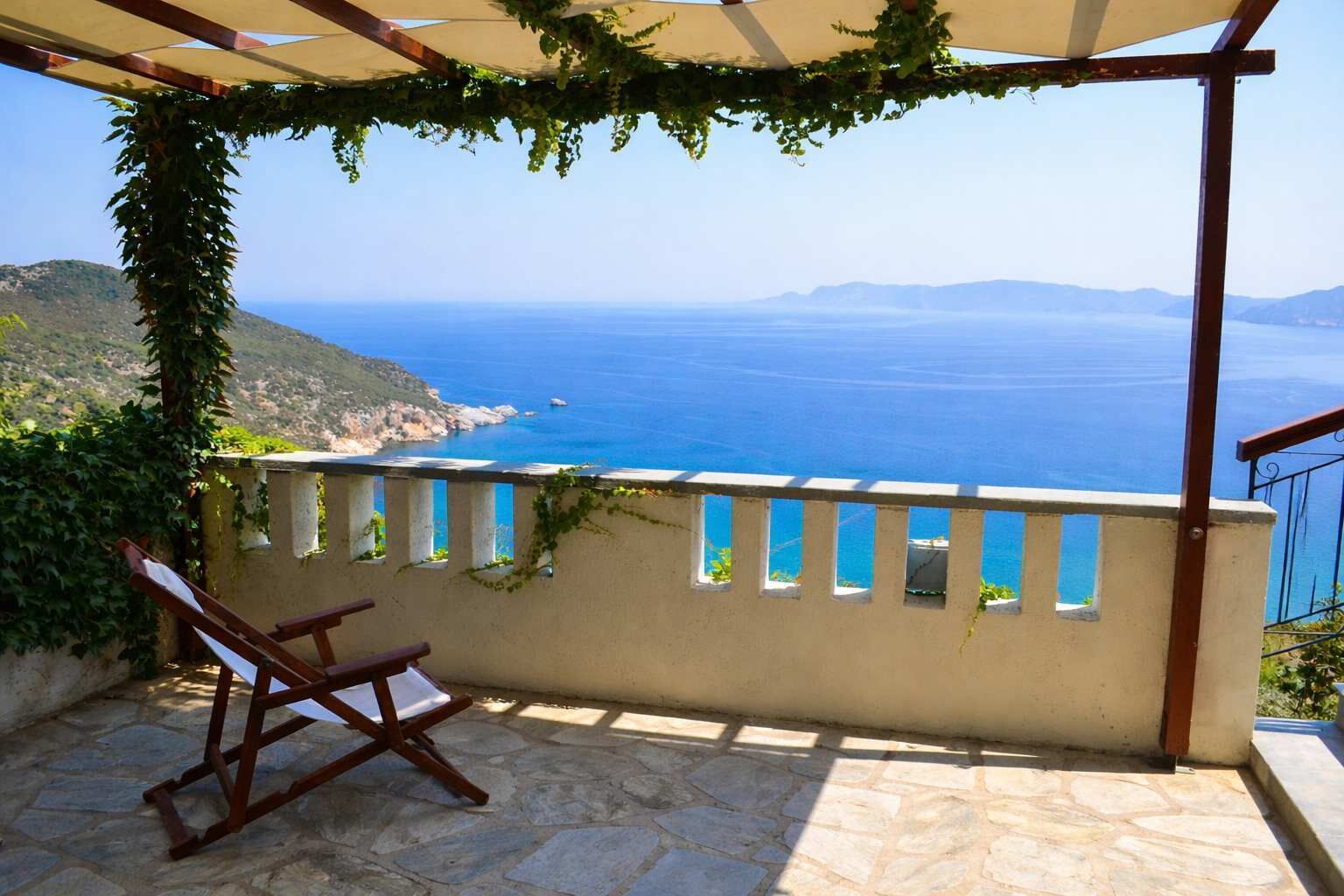 Une terrasse en pierre avec une chaise en bois, une pergola couverte de plantes grimpantes et une vue sur la mer et les collines lointaines.