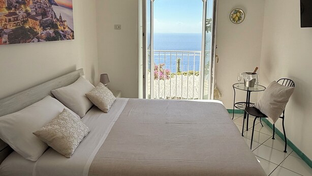 Quarto com cama, vista para o mar, varanda e um quadro na parede.