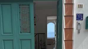 Uma porta azul-turquesa com uma janela decorativa, uma escadaria que leva a uma varanda e uma placa indicando que o imóvel é uma 'Turino House'.