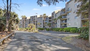 En flervåningsbostadsbyggnad med balkonger, en asfalterad uppfart och omgivande grönska.