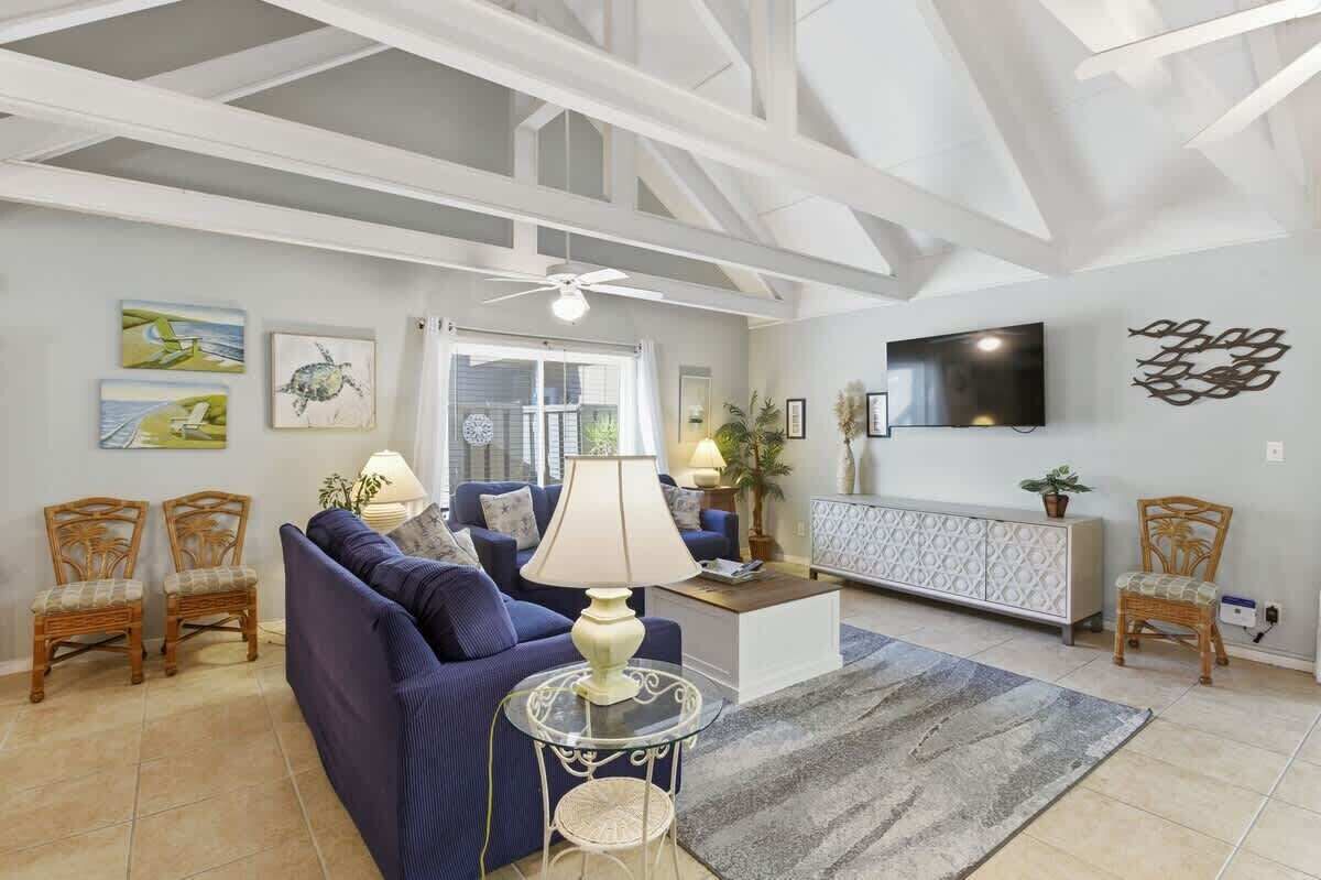 Una sala de estar con sofá, sillas, televisión, obras de arte y un ventilador de techo.