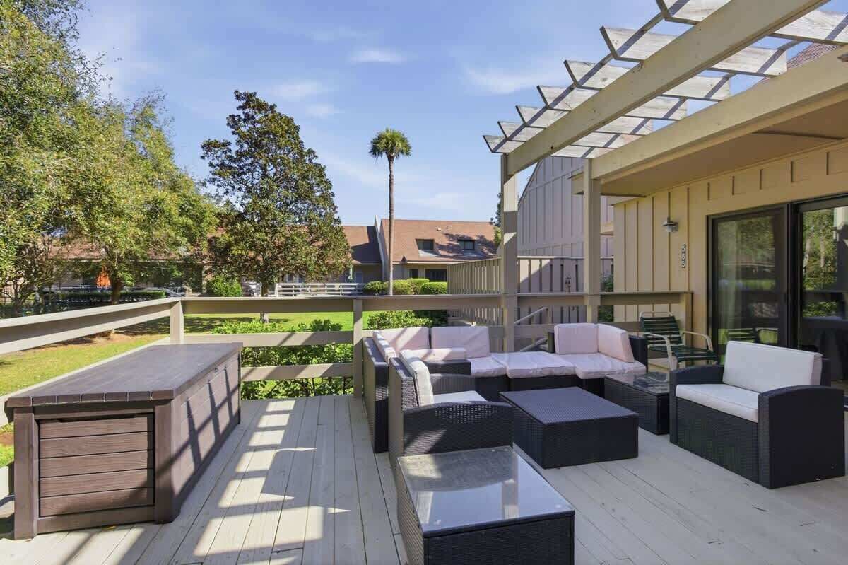 An outdoor deck with wicker furniture, a wooden bench, and a pergola structure.