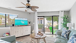 A living room with a ceiling fan, a television, a sofa, a coffee table, and a view of the outdoors. - Crystal Village II 26A (Miramar Beach)