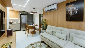 A modern living room with a sofa, a dining area with chairs, a kitchen with cabinets, and an air conditioning unit. - Master Luxo Jardins Almare - By Almare (João Pessoa)